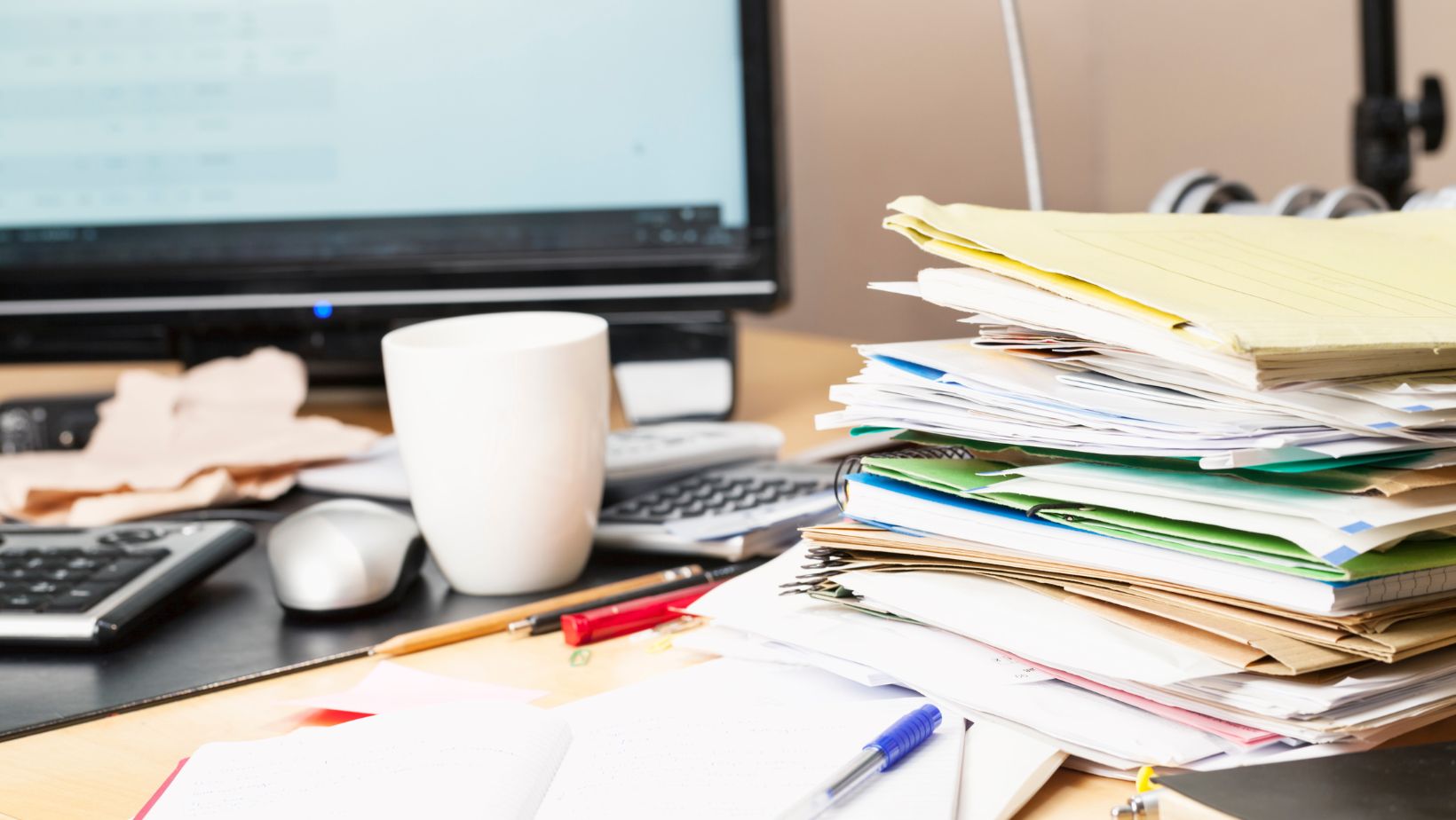 An unorganized desk with paperwork and a coffee mug.
