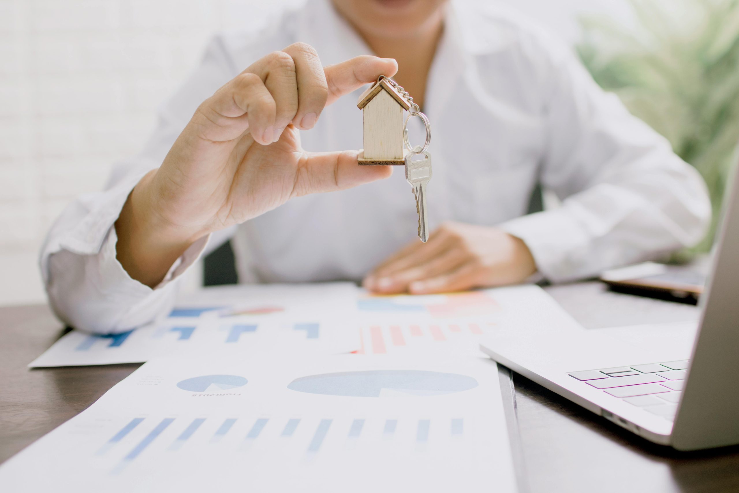 Woman sitting at a table with paperwork and an open laptop, she's holding a keychain of a small wooden house.