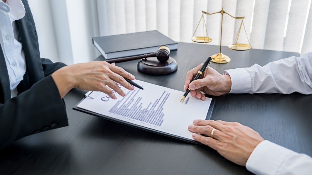 Two people in business attire review and discuss a legal document at a desk, featuring a gavel and scales of justice, conveying a formal tone.