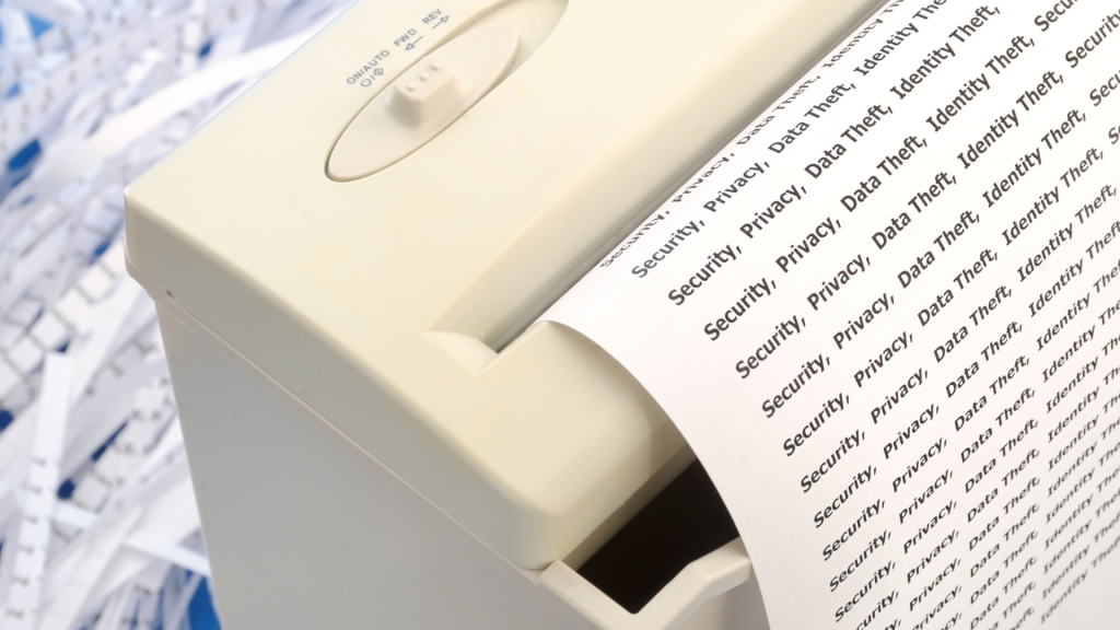 Close-up of a paper shredder in action. The paper shows words like "Security" and "Privacy." Shredded paper strips are visible, highlighting data protection.