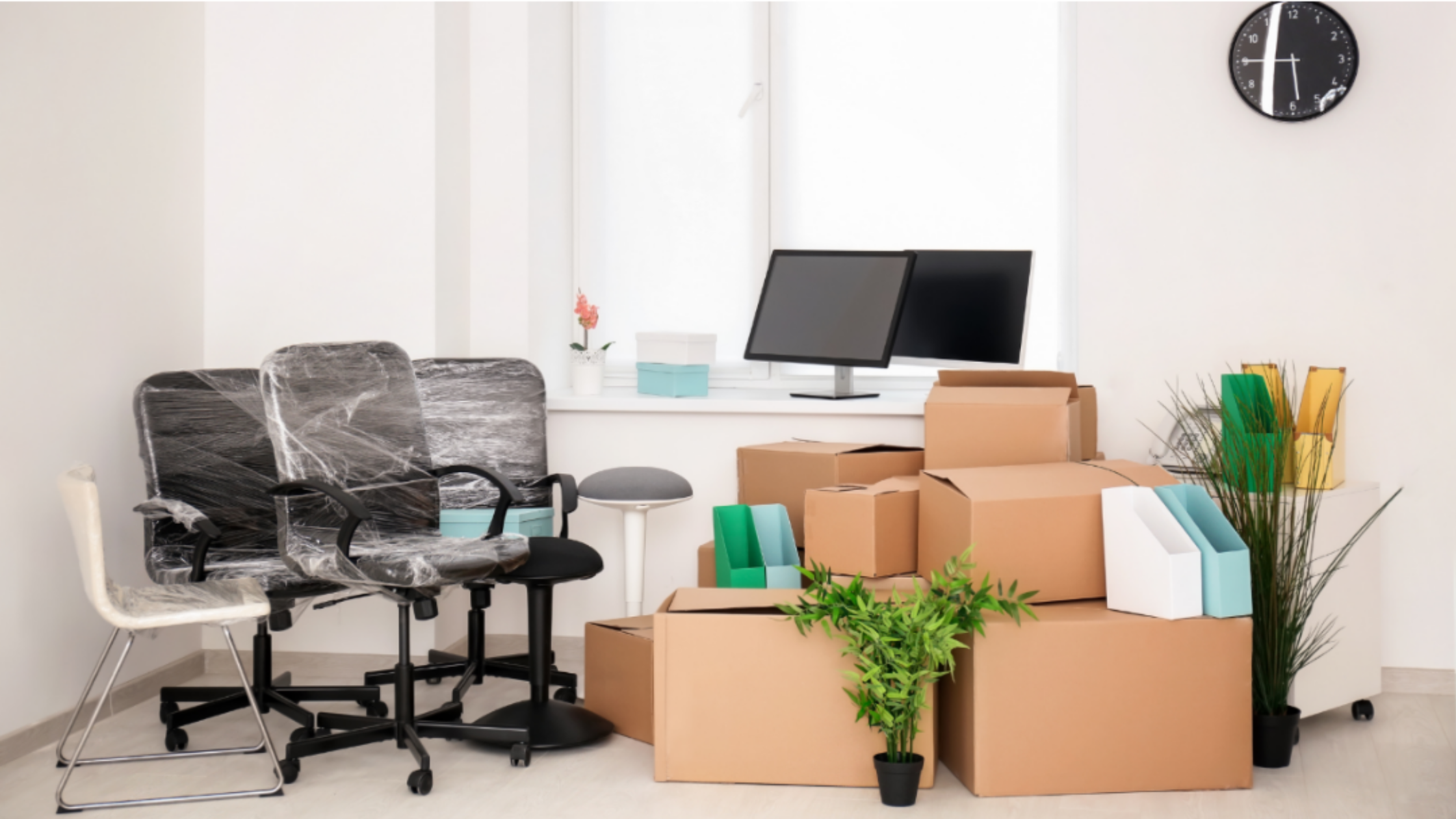 Office packed for a move with wrapped chairs, computer monitors, and cardboard moving boxes.